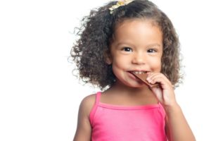 Joyful little girl with an afro hairstyle eating a chocolate bar isolated on white