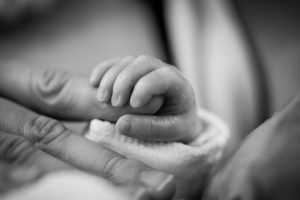 Hand eines frisch geborenen Babys umschließt den Finger der Mutter