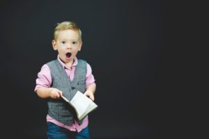 kleiner Junge hält mit offenem Mund ein Buch in der Hand