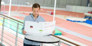 junger Mann vor einem Sportplatz studiert ein Papier