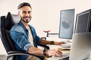 ein junger Mann am Schreibtisch mit Monitoren und Laptop