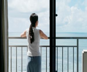 junge Frau schaut vom Balkon aufs Meer