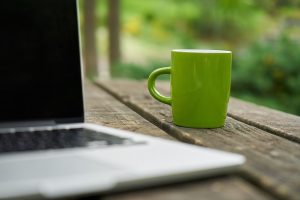 Grüne Tasse hinter einem Laptop auf Gartentisch