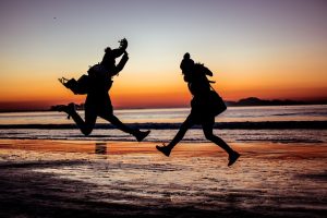 zwei Menschen am Strand springen vor dem Sonnenuntergang