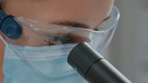 Auge mit Schutzbrille schaut durch ein Mikroskop
