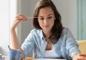 Junge Frau denkt mit einem Stift an der Schläfe