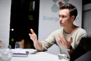 Junger Mann am Tisch vor einem Plakat von emergencyeye